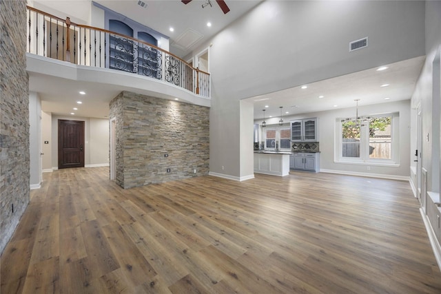 unfurnished living room featuring ceiling fan, wood-type flooring, and a high ceiling