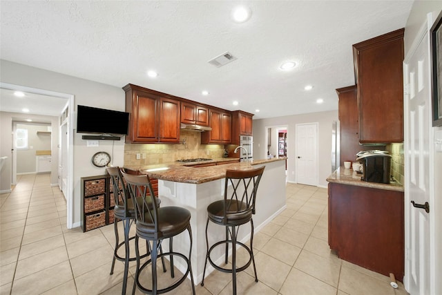 kitchen featuring backsplash, light stone countertops, light tile patterned floors, and a kitchen breakfast bar