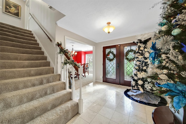 foyer with french doors, an inviting chandelier, and crown molding