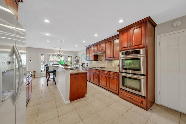 kitchen with backsplash, stainless steel appliances, a kitchen island with sink, decorative light fixtures, and a notable chandelier