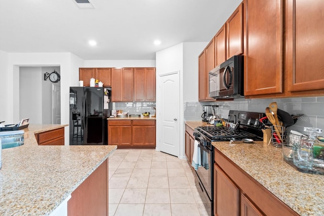 kitchen featuring light tile patterned flooring, backsplash, light stone counters, and black appliances