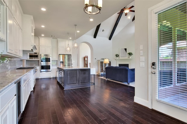 kitchen featuring white cabinetry, light stone countertops, backsplash, an island with sink, and decorative light fixtures