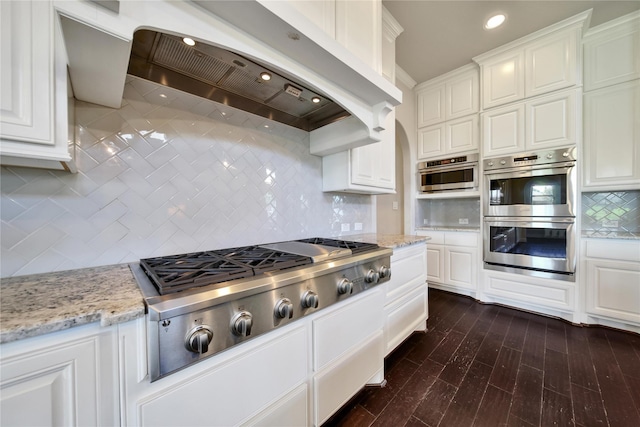 kitchen with backsplash, ventilation hood, white cabinetry, and stainless steel appliances