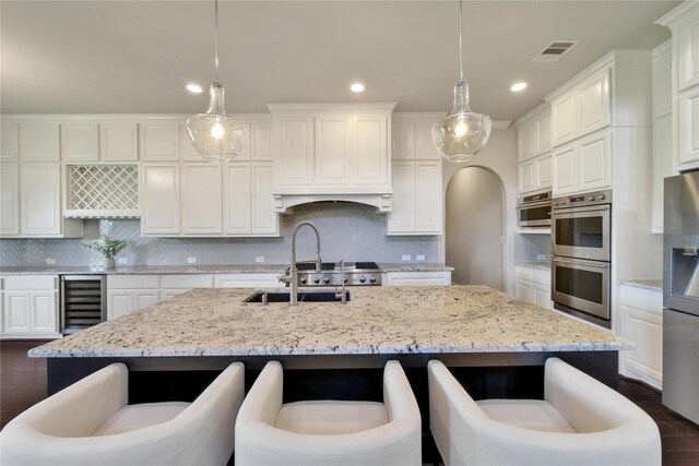 kitchen with pendant lighting, an island with sink, beverage cooler, and stainless steel appliances