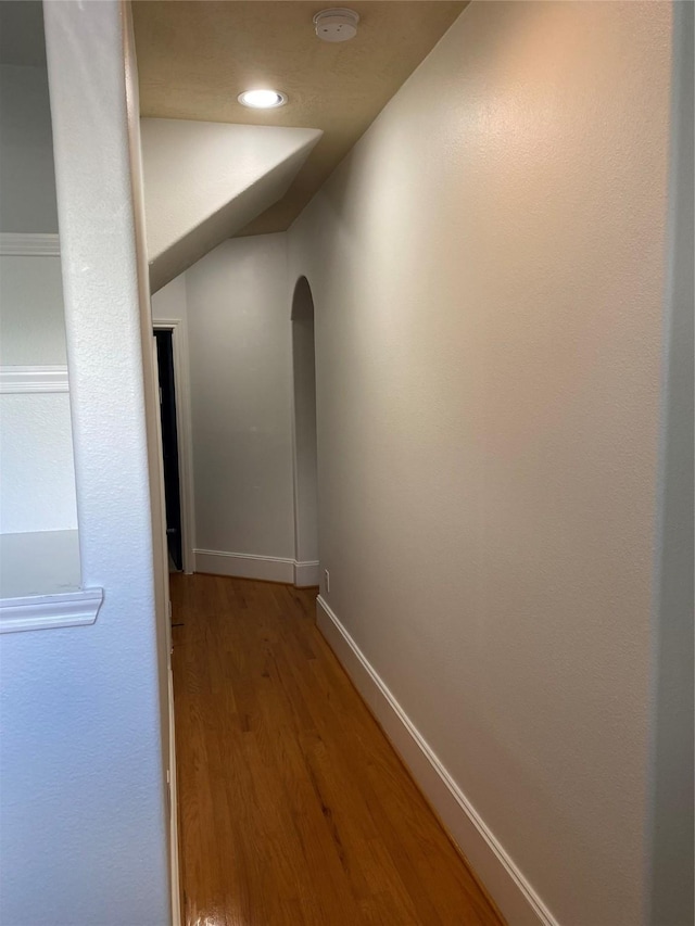 hallway with arched walkways, light wood-style flooring, recessed lighting, baseboards, and vaulted ceiling