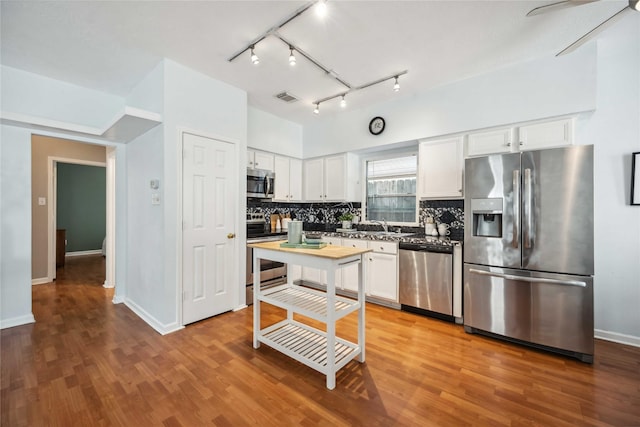 kitchen featuring hardwood / wood-style flooring, decorative backsplash, white cabinetry, and appliances with stainless steel finishes