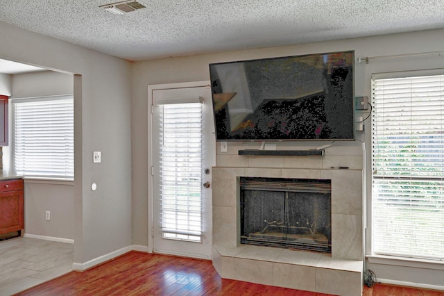 living room with a tile fireplace, a textured ceiling, and light wood-type flooring