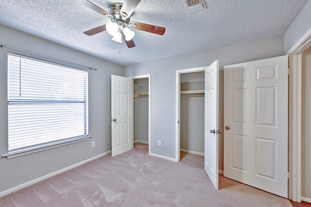 unfurnished bedroom featuring multiple windows, two closets, light colored carpet, and ceiling fan