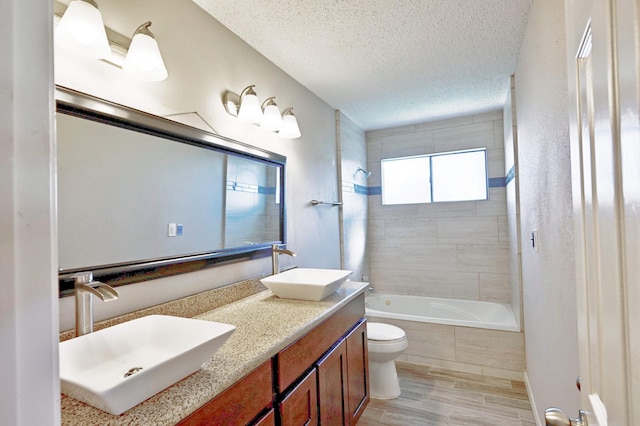 full bathroom featuring tiled shower / bath, a textured ceiling, toilet, vanity, and hardwood / wood-style flooring