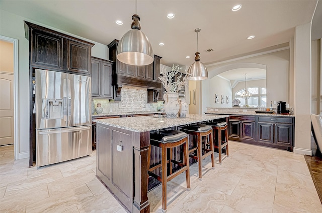 kitchen with stainless steel refrigerator with ice dispenser, light stone countertops, decorative light fixtures, a kitchen island, and dark brown cabinetry