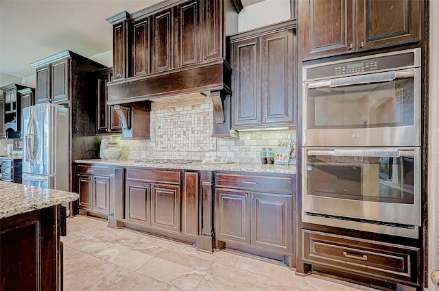 kitchen with decorative backsplash, dark brown cabinets, stainless steel appliances, and light stone counters