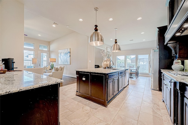 kitchen with light stone countertops, sink, stainless steel appliances, decorative light fixtures, and a center island with sink