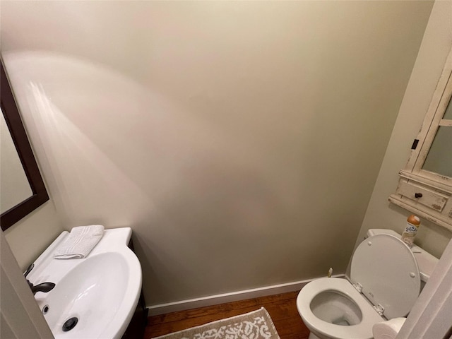 half bath featuring wood finished floors, a sink, toilet, and baseboards