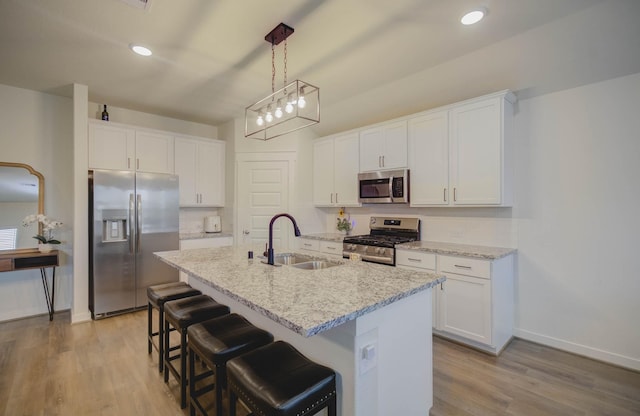 kitchen featuring a kitchen island with sink, white cabinets, sink, light stone counters, and stainless steel appliances