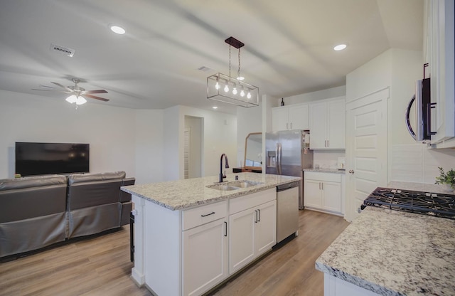 kitchen with an island with sink, sink, white cabinets, and hanging light fixtures