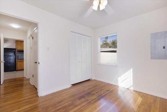 unfurnished bedroom with hardwood / wood-style flooring, ceiling fan, black refrigerator, and electric panel