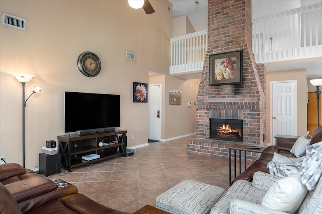 living room with ceiling fan, light tile patterned floors, a high ceiling, and a brick fireplace