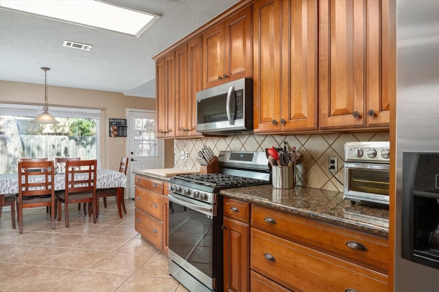 kitchen with dark stone counters, hanging light fixtures, light tile patterned floors, appliances with stainless steel finishes, and tasteful backsplash