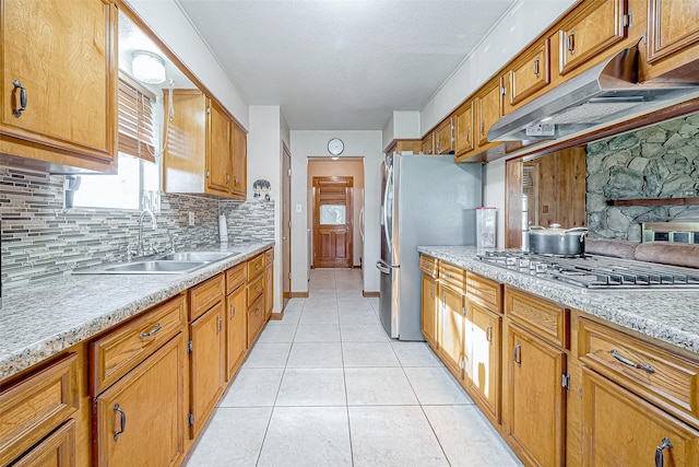 kitchen featuring sink, a stone fireplace, decorative backsplash, light tile patterned floors, and appliances with stainless steel finishes