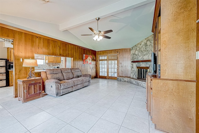 living room with ceiling fan, lofted ceiling with beams, wooden walls, a fireplace, and light tile patterned flooring