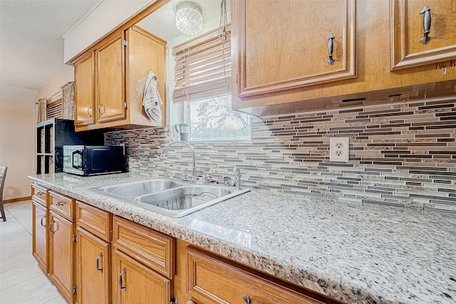 kitchen with decorative backsplash, light tile patterned floors, light stone counters, and sink