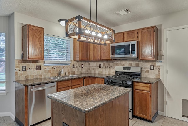 kitchen with appliances with stainless steel finishes, a textured ceiling, sink, pendant lighting, and a kitchen island