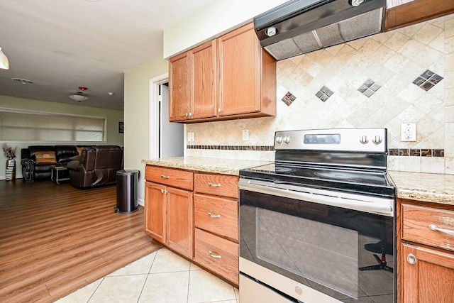 kitchen featuring decorative backsplash, light stone counters, light tile patterned floors, stainless steel electric range oven, and range hood