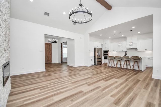 living room with beam ceiling, sink, a notable chandelier, a fireplace, and light wood-type flooring