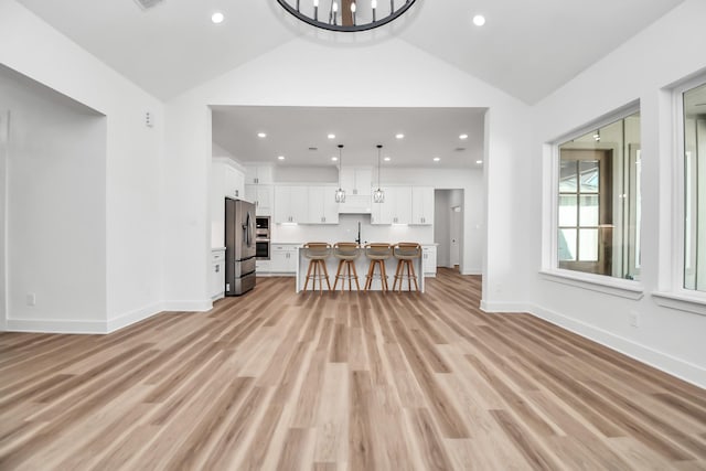 unfurnished living room with light hardwood / wood-style flooring, vaulted ceiling, and sink