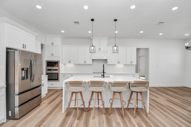 kitchen with stainless steel appliances, decorative light fixtures, a kitchen island with sink, white cabinets, and light wood-type flooring