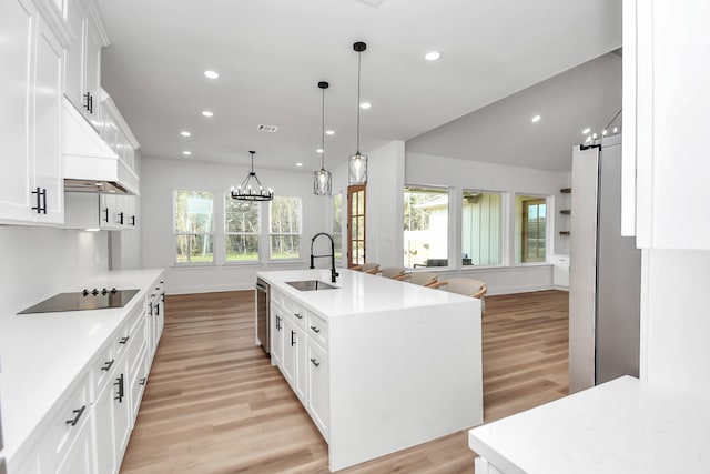 kitchen with black electric stovetop, sink, hanging light fixtures, an island with sink, and white cabinetry