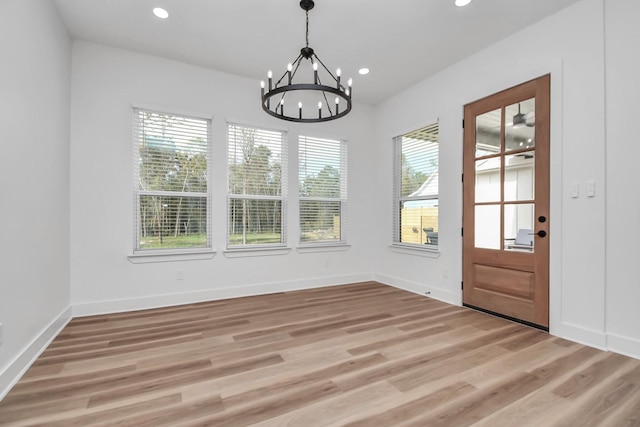 unfurnished dining area with ceiling fan with notable chandelier, a healthy amount of sunlight, and light hardwood / wood-style floors