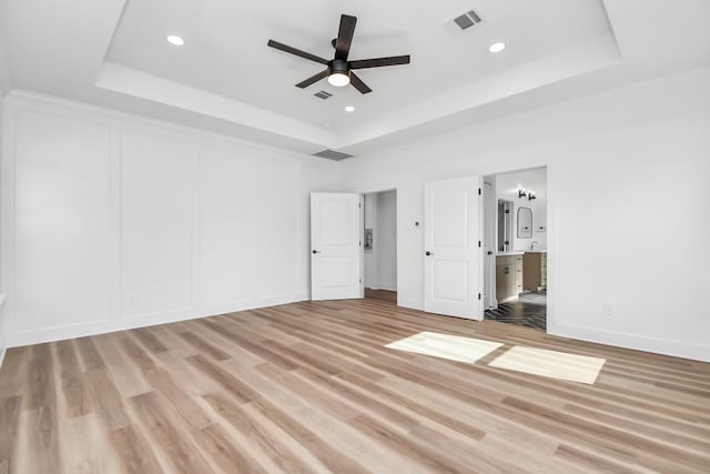 unfurnished bedroom with a raised ceiling, ensuite bathroom, light hardwood / wood-style flooring, and ceiling fan