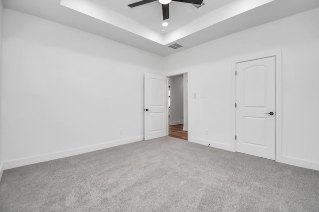 empty room with carpet, ceiling fan, and a raised ceiling