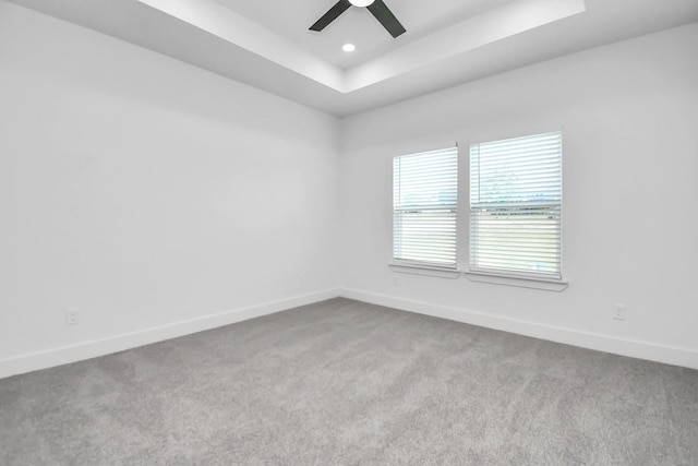 spare room with ceiling fan, a raised ceiling, and light colored carpet