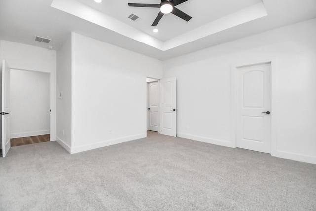 unfurnished bedroom featuring light carpet, a tray ceiling, and ceiling fan