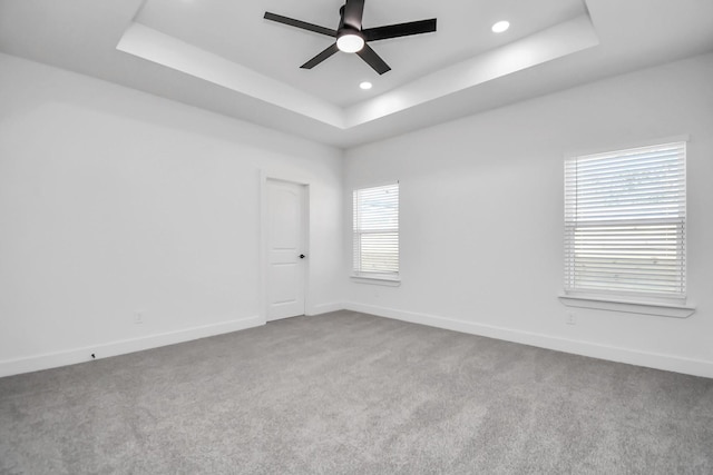 carpeted empty room with a raised ceiling and ceiling fan