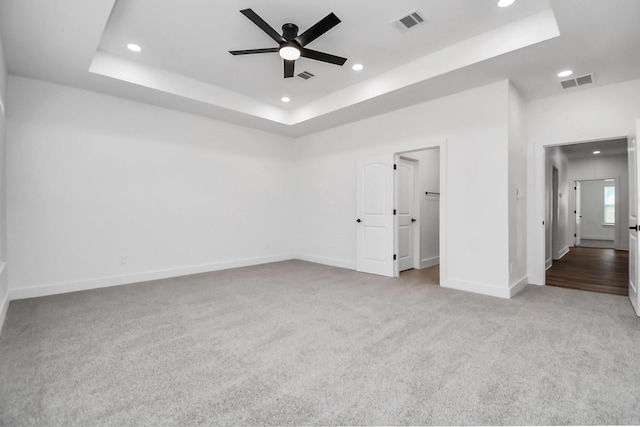 unfurnished room with a raised ceiling, ceiling fan, and light colored carpet