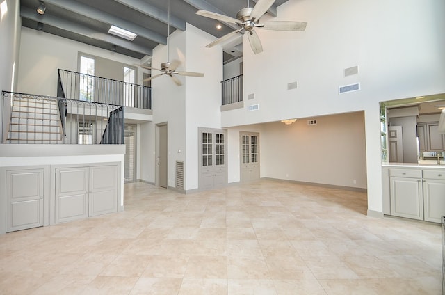 unfurnished living room with ceiling fan, beamed ceiling, a towering ceiling, and sink