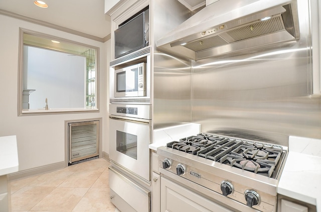 kitchen featuring appliances with stainless steel finishes, white cabinetry, crown molding, and wall chimney range hood