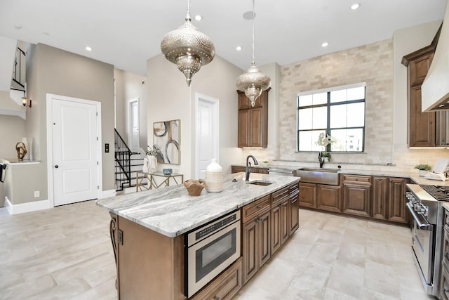 kitchen featuring high end range, a kitchen island with sink, sink, hanging light fixtures, and light stone counters