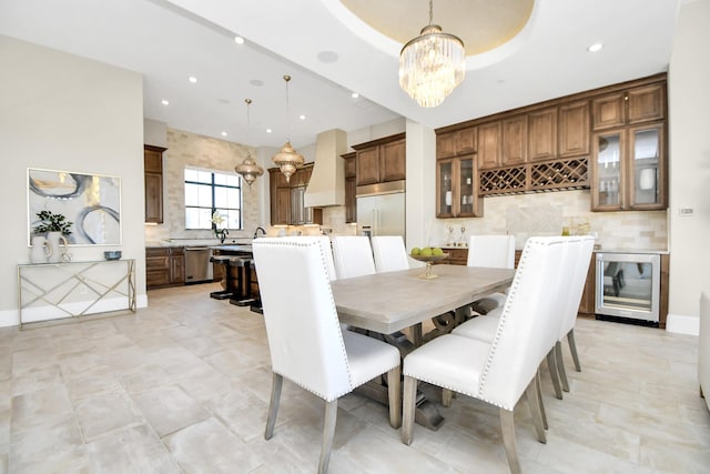 dining area with a raised ceiling, beverage cooler, and a notable chandelier