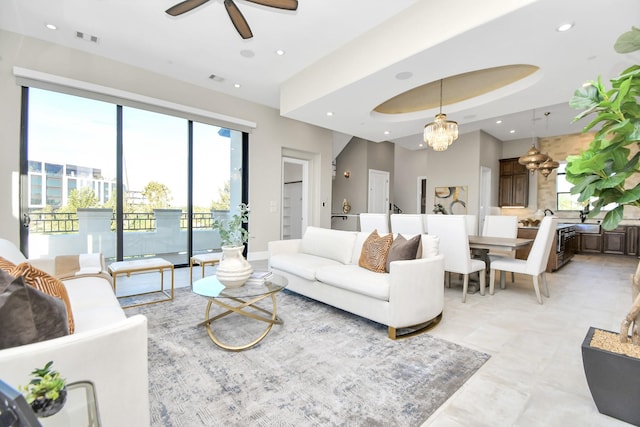 living room featuring a tray ceiling and ceiling fan with notable chandelier