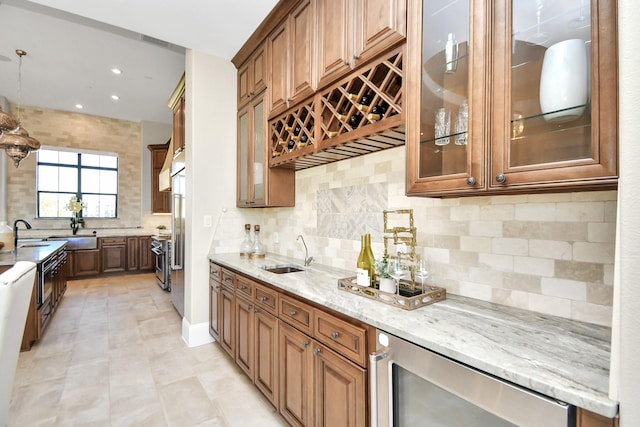 kitchen featuring light stone countertops, decorative backsplash, beverage cooler, sink, and hanging light fixtures