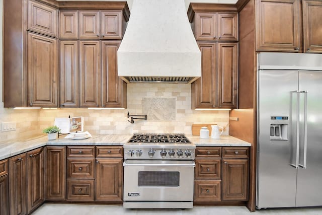 kitchen with backsplash, light stone counters, custom range hood, and premium appliances