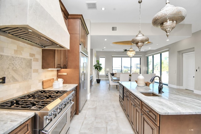 kitchen with custom exhaust hood, sink, built in appliances, light stone countertops, and tasteful backsplash