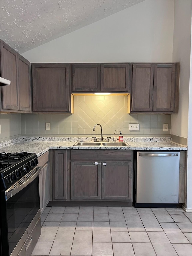 kitchen with lofted ceiling, sink, light stone countertops, appliances with stainless steel finishes, and light tile patterned flooring