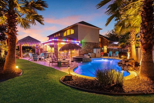 pool at dusk featuring a fire pit, a lawn, a gazebo, an in ground hot tub, and a patio area