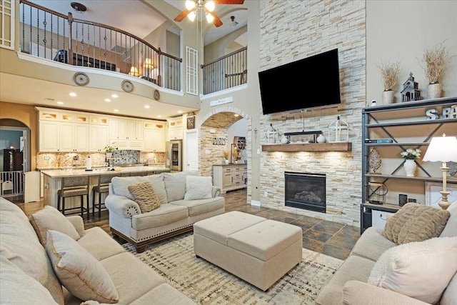 living room with ceiling fan, a fireplace, and a high ceiling