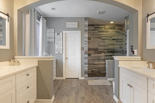 bathroom with wood-type flooring, vanity, and a tile shower